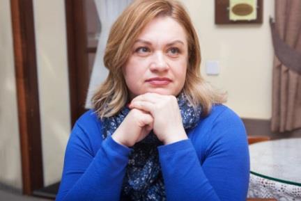 Žena ozbiljnog lica u plavoj majici naslonjena na ruke