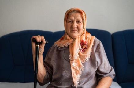 Baba sa maramom na glavi i štapom za hodanje sedi na krevetu