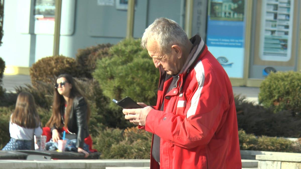 Penzioner stoji na ulici i gleda u telefon
