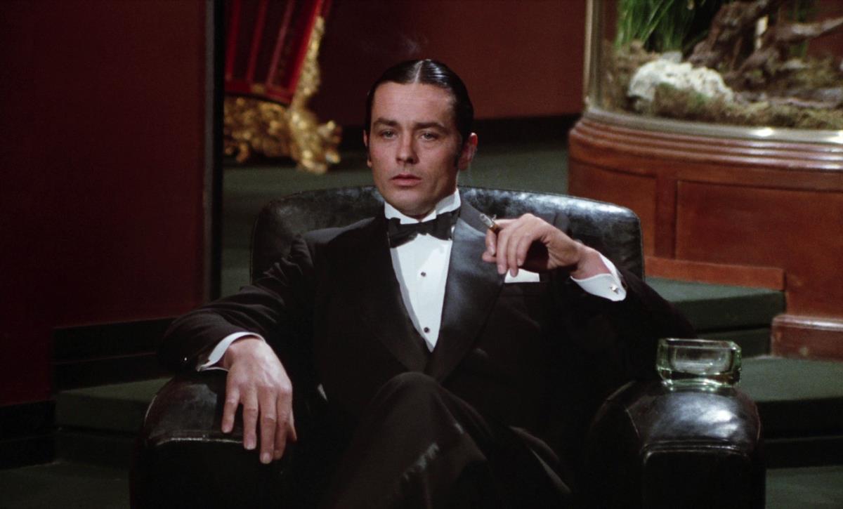 Alen Delon u smokingu sedi u kožnoj fotelji i puši