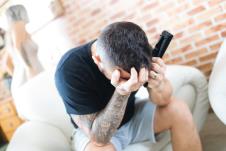 Mladić sedi na krevetu i drži ruke na glavi