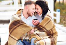 stockphotoyoungcoupleembracingandcoveredwithawarmblanketsittingonautumnbeachanddrinkcoffee560826904.jpg