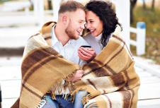 stockphotoyoungcoupleembracingandcoveredwithawarmblanketsittingonautumnbeachanddrinkcoffee560826904.jpg