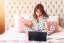 stockphotoserioushispanicwomanworkingonherlaptopsittingonherbedathomewearingpajamas1716910303.jpg