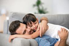 stockphotohappyfatherhuggingcutelittlegirllyingtogetherrestingoncomfortablesofasmilingdad1276179043-08-05-2020.jpg