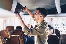 stockphotogoodlookingyoungmanputtinghandluggageinthetopshelfinthebus1500997055.jpg