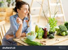 stockphotoyoungandhappywomaneatinghealthysaladsittingonthetablewithgreenfreshingredientsindoors622381814.jpg