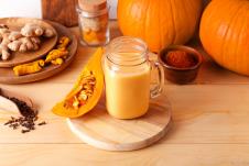 Sok od bundeve u teglici na drvenoj dasci okružen drugim bundeva i začinima na stolu