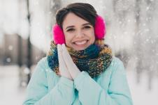 Nasmejana devojka sa štitnicima na ušima, uživa u zimi i snegu