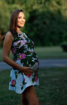 Aleksandra Prijović u cvetnoj haljini, drži trudnički stomak i pozira u parku