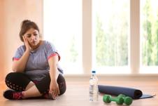 žena s viškom kilograma gleda bez motivcije u tegove za vežbanje