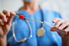 medicinski radnik u plavom odelu sa stetoskopom ubacuje u epruvetu štapić sa uzorkom za bris