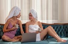 Dve devojke umotane u peškire sede na kauču i piju kafu