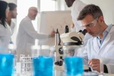 naučnik u belom mantilu u laboratoriji sa providnim zaštitnim naoračima gleda kroz mikroskop