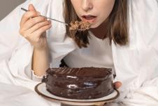 mlada žena jede ćokoladnu tortu u krevetu