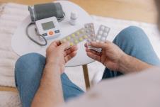 čovek gleda različite lekove dok ispred njega stoji merač za pritisak