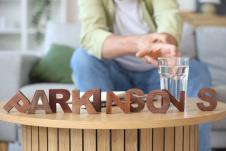 muškarac pridržava drhtavu ruku pruženu ka čaši vode, na stolu natpis Parkinsonova bolest