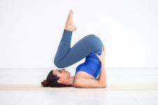 žena u plavom trikou izvodi joga pozu pawanmuktasana