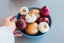 ruka žene dodiruje činiju punu različih vrsta luka, plava pozadina