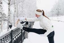 devojka u opremi za vežbanje radi vežbe istezanja nogu na ogradi u parku koji je prekriven snegom
