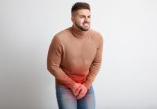 muškarac sa bradicom koji stoji se drži za predeo prepona koji je označen crvenom bojom