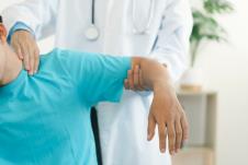 muškarac u plavoj majci sa kratkim rukavima na pregledu kod lekara koji mu drži podignutu levu ruku i pregleda mišiće vrata