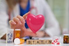 medicinski radnik drži figuricu srca iznad stola na kom su lekovi i ispis statini na drvenim kockicama
