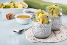 dve teglice sa čija pudingom i voćem na vrhu, kašičica, činija sa medom i iseckano voće u pozadini