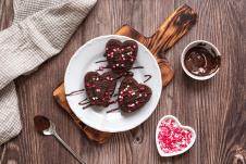 tri čokoladnna medenjaka na tanjiru na drvenom stolu, činija sa istopljenom čokoladom i mrvicama u obliku srca