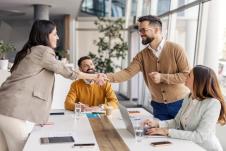 četiri osobe u sali za sastanke od kojih se dve rukuju uz osmeh