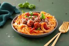 ćuftice u paradajz sosu sa špagetama na azelenom stolu, zlatna kašika i viljuška pored