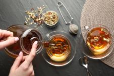 prikaz ženskih ruku sa staklenim čajnikom iz kog sipa čaj u providnu staklenu šuoljicu pored koje je druga staklena šoljica sa čajem