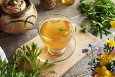 providna šolja čaja sa svežim biljkama pored i prolećnim cvećem