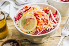 činija salate od kupusa, cvekle i šargarepe sa kriškom limuna na drvenom stolu