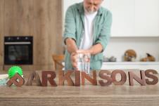 muškarac pridržava drhtavu ruku pruženu ka čaši vode, na stolu natpis Parkinsonova bolest