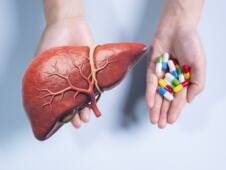 muškarac drži model jetre u jednoj ruci i šaku lekova u drugoj