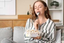 devojka sedi u dnevnoj sobi na kauču i jede sladoled iz kutije kašikom