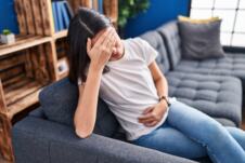 mlada žena na kauču se drži za glavu i stomak