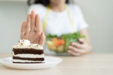 žena odbija parče torte jednom rukom, drugom pridržava činiju sa salatom