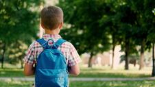 đak prvak na putu do škole nosi ranac, podgled s leđa, ispred park