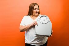 žena sa viškom kilograma drži vagu u rukama, narandžasta pozadina