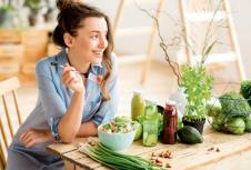 stockphotoyoungandhappywomaneatinghealthysaladsittingonthetablewithgreenfreshingredientsindoors622381814.jpg