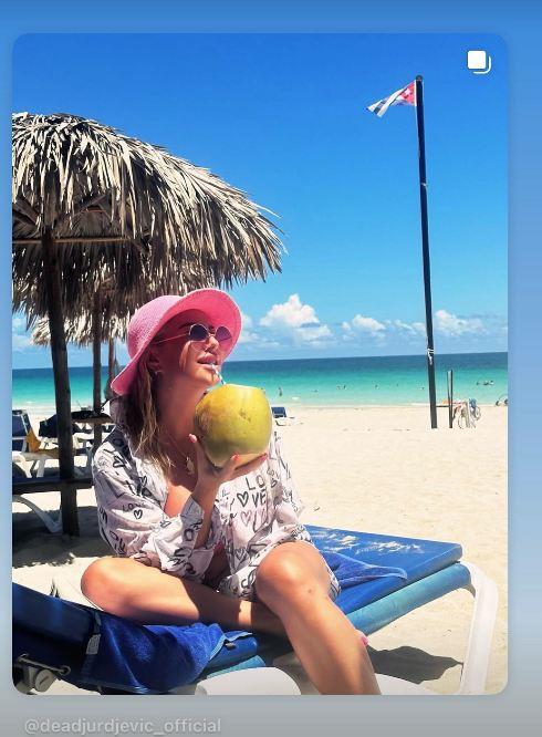Dea Đurđević na plaži na Kubi, sedi na ležaljci i pije kokosovu vodu, u roze šeširu i naočarima za sunce