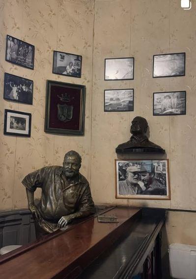 Enterijer sa skulpturom Ernesta Hemingveja oslonjenog na šank, okružen fotografijama i bistom na zidu