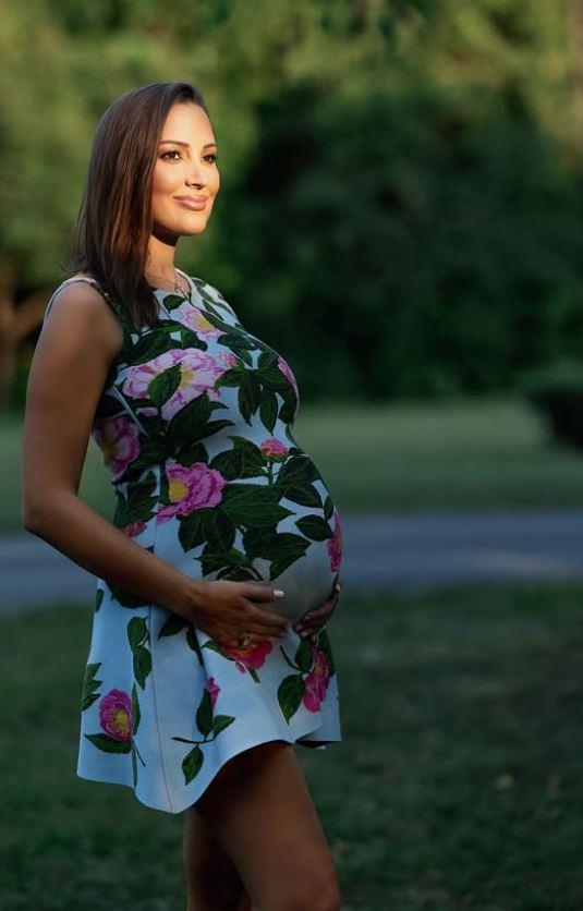 Aleksandra Prijović u cvetnoj haljini, drži trudnički stomak i pozira u parku