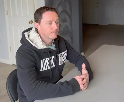 Džastin Dorf u sivom duksu sedi za stolom.jpg