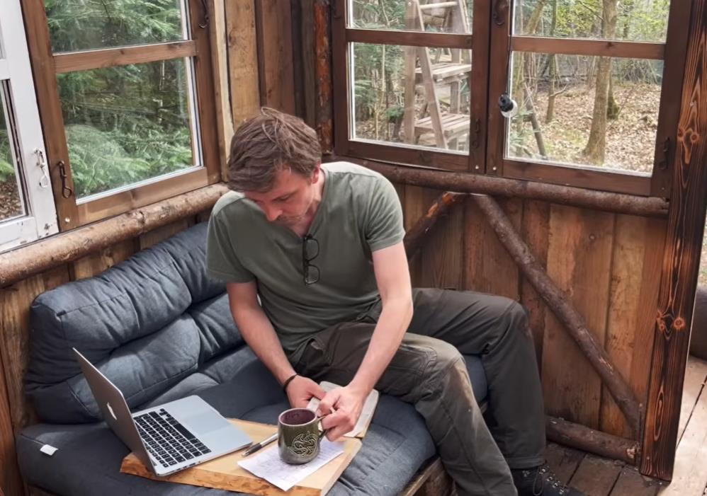 Andres Bojzen pije kafu kraj laptopa u drvenoj kući u šumi.jpg