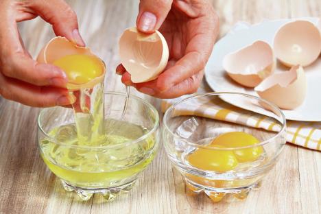 stockphotowomanhandsbreakinganeggtoseparateeggwhiteandyolksandeggshellsatthebackground468388310.jpg