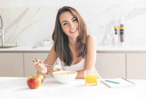 stockphotosmilinghealthywomaneatingcornflakescerealwhilesittingandhavingbreakfastatthekitchen710625991.jpg