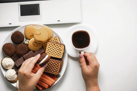 stockphotobadnutritionhabitsovereatingconceptwomaneatingcookiesatworkplaceyounggirlsnacking1475028836.jpg